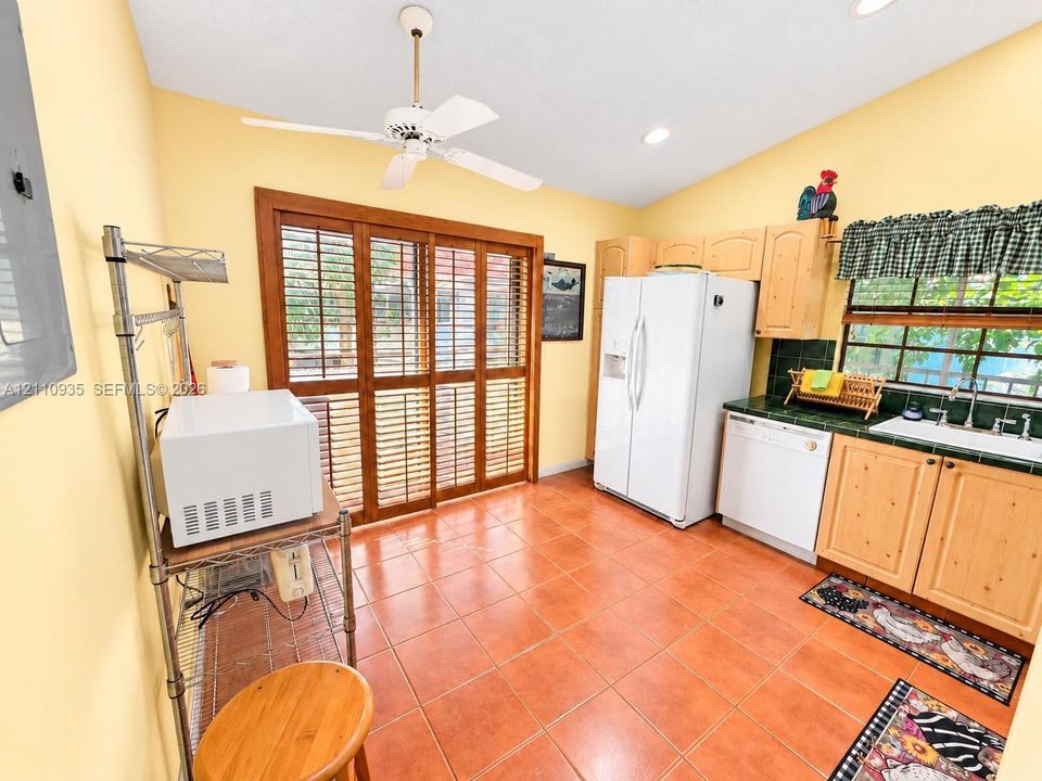 Kitchen featuring ceramic tile flooring, light wood cabinetry, built-in recessed lighting, white appliances, and wood-framed sliding glass doors