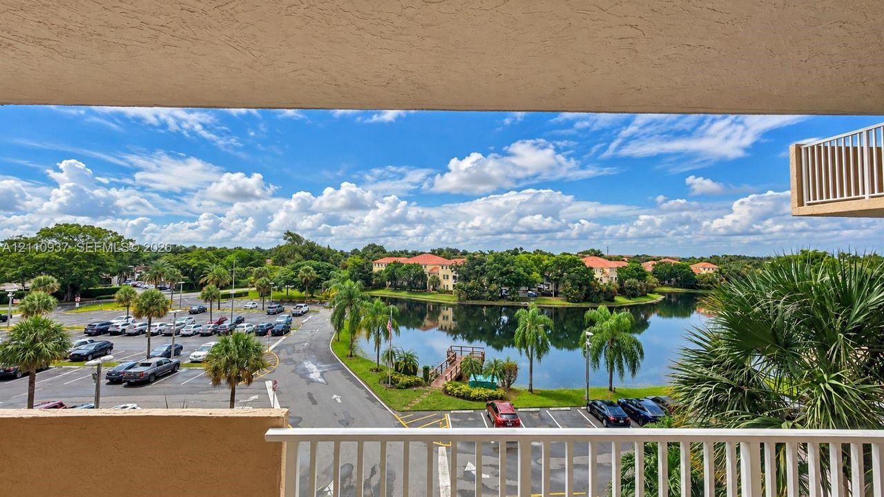 Covered balcony with white metal railing overlooking a landscape featuring a natural pond, mature palm trees, and established greenery