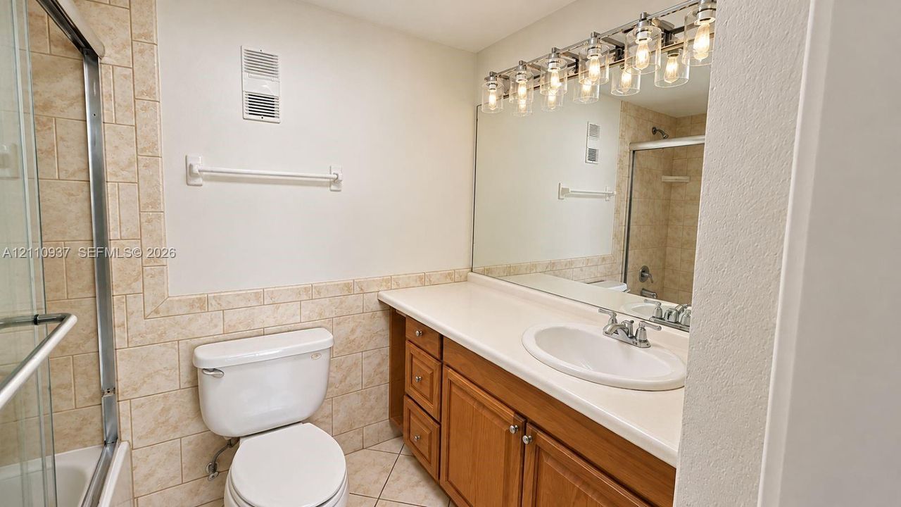 Bathroom featuring a wood vanity with a solid-surface countertop, an integrated oval sink, ceramic tile wainscoting, and a multi-light fixture over a wall-to-wall mirror