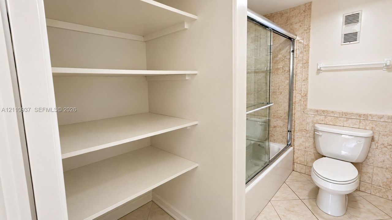 Built-in storage shelving, walk-in shower with a sliding glass door, ceramic tile surround, and tile flooring