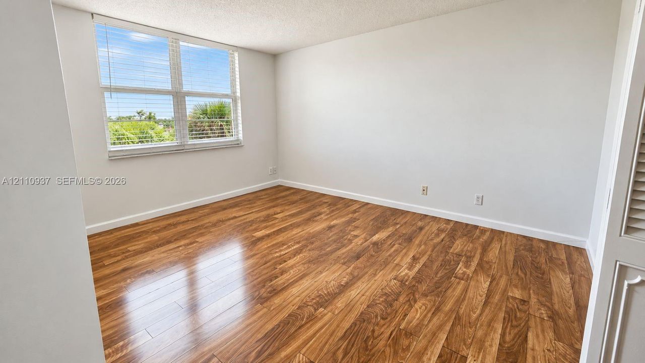 Room featuring wood-finish flooring, a large window, neutral wall paint, and louvered closet doors