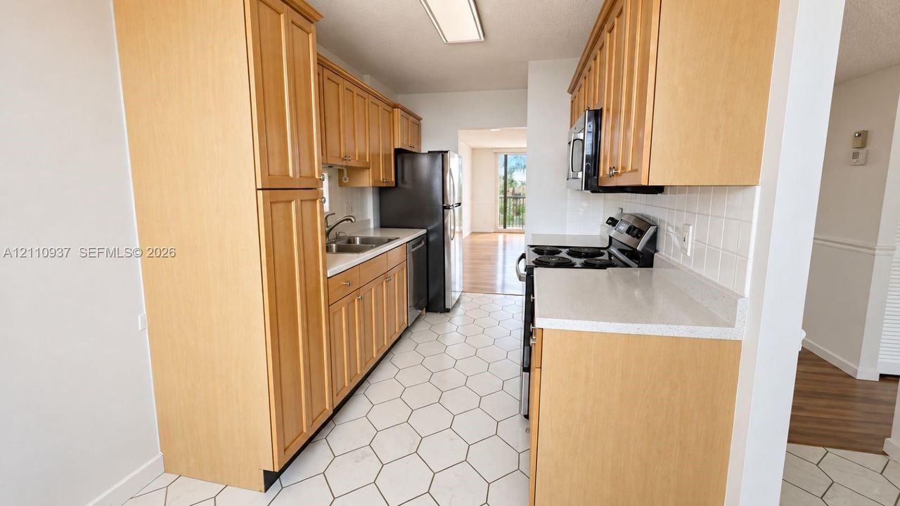 Kitchen featuring light-finish cabinetry, white solid-surface countertops, white hexagonal floor tile, stainless steel appliances, and a square tile backsplash