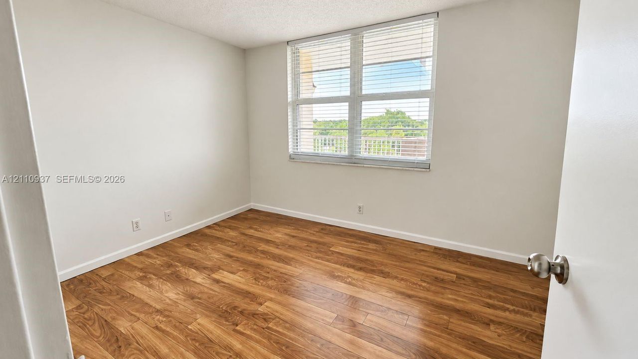 Interior space featuring wood-finish flooring, neutral wall tones, and a large multi-pane window with horizontal blinds