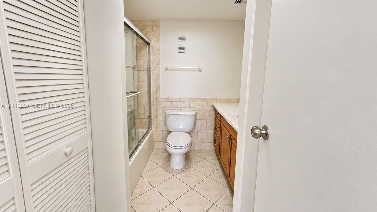 Bathroom featuring wood-finish cabinetry, neutral-toned tiled flooring laid on a diagonal, a glass-enclosed shower with tiled walls, and louvered closet doors