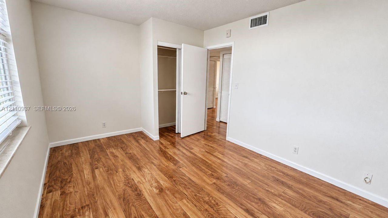 Room featuring wood-finish flooring, neutral wall paint, and a built-in closet with an interior shelf and rod