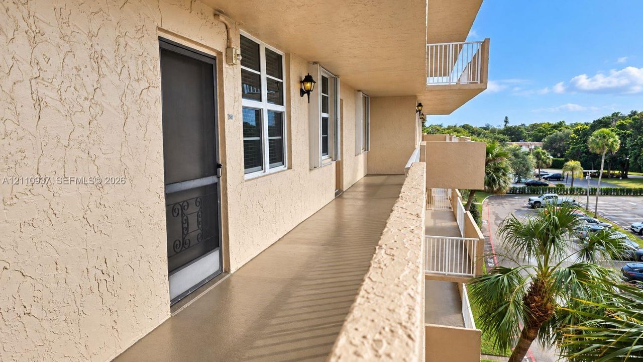 Exterior walkway featuring a stucco facade, metal screen door, white-framed multi-pane windows, wall-mounted coach lighting, and a white railing