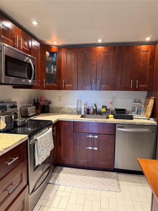 Kitchen featuring dark wood-finish cabinetry, stone-style countertops, stainless steel appliances, recessed ceiling lighting, and tile flooring