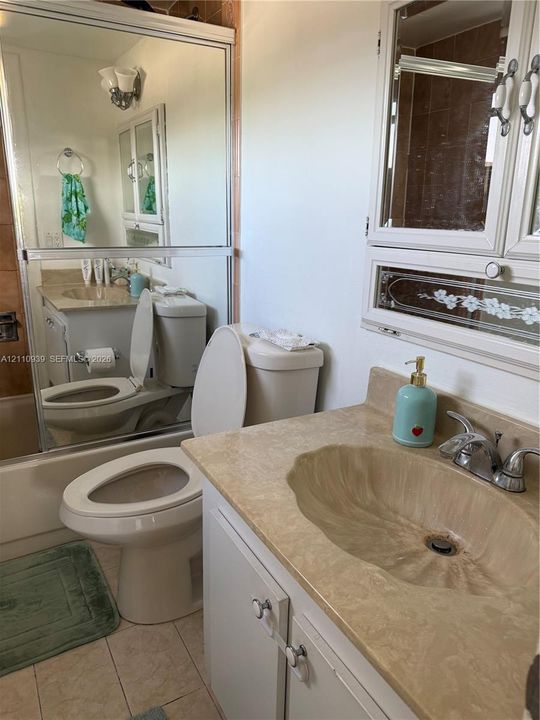 Vanity featuring an integrated molded sink, stone-finish countertop, and chrome dual-handle faucet, complemented by a large wall-mounted mirror and a built-in recessed medicine cabinet with decorative glass detailing