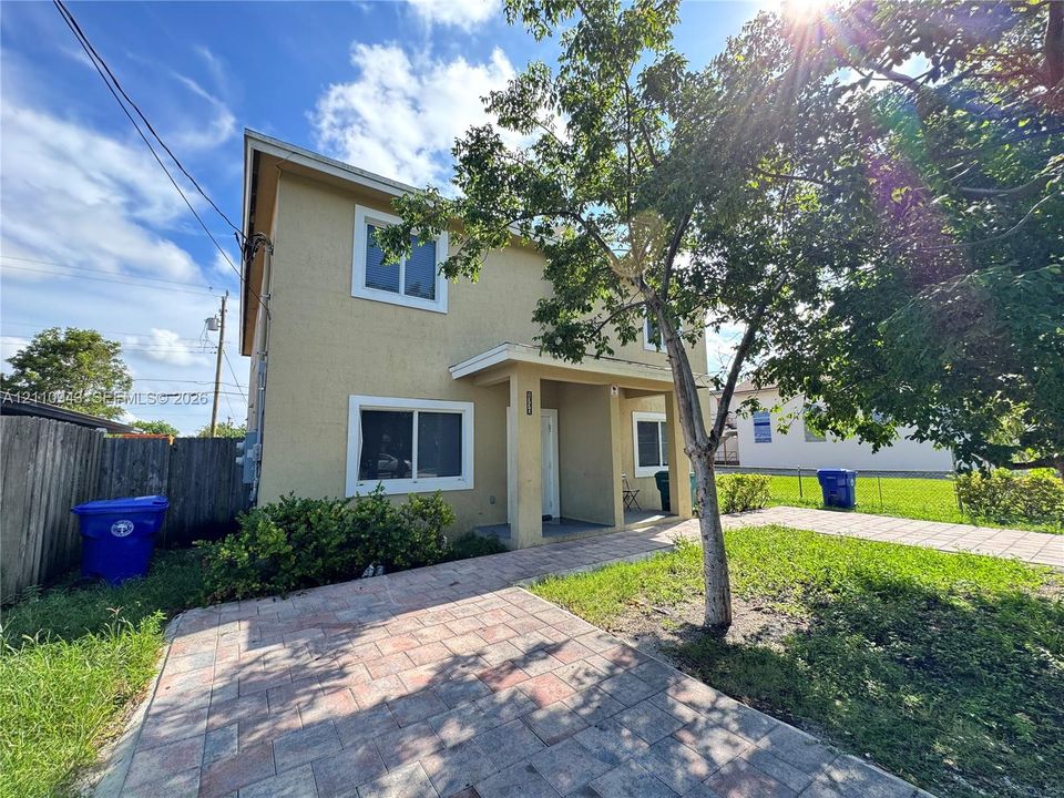 Two-story exterior featuring a stucco facade, covered front entryway, paved driveway, and established landscaping