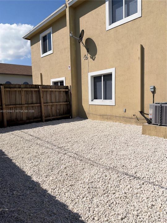Exterior area featuring a gravel-surfaced yard, wood-style privacy fencing, and a stucco-finished exterior wall