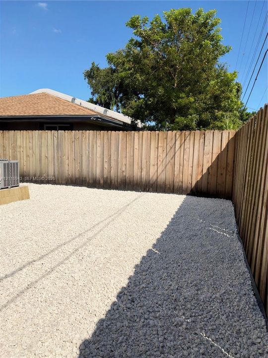Rear yard featuring a gravel surface, wood privacy fencing, and mature tree