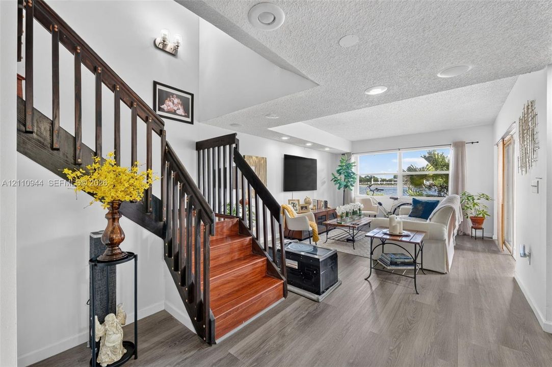 Open-concept living space featuring wood-finish flooring, staircase with dark-stained wood railings and treads, recessed lighting, and large windows