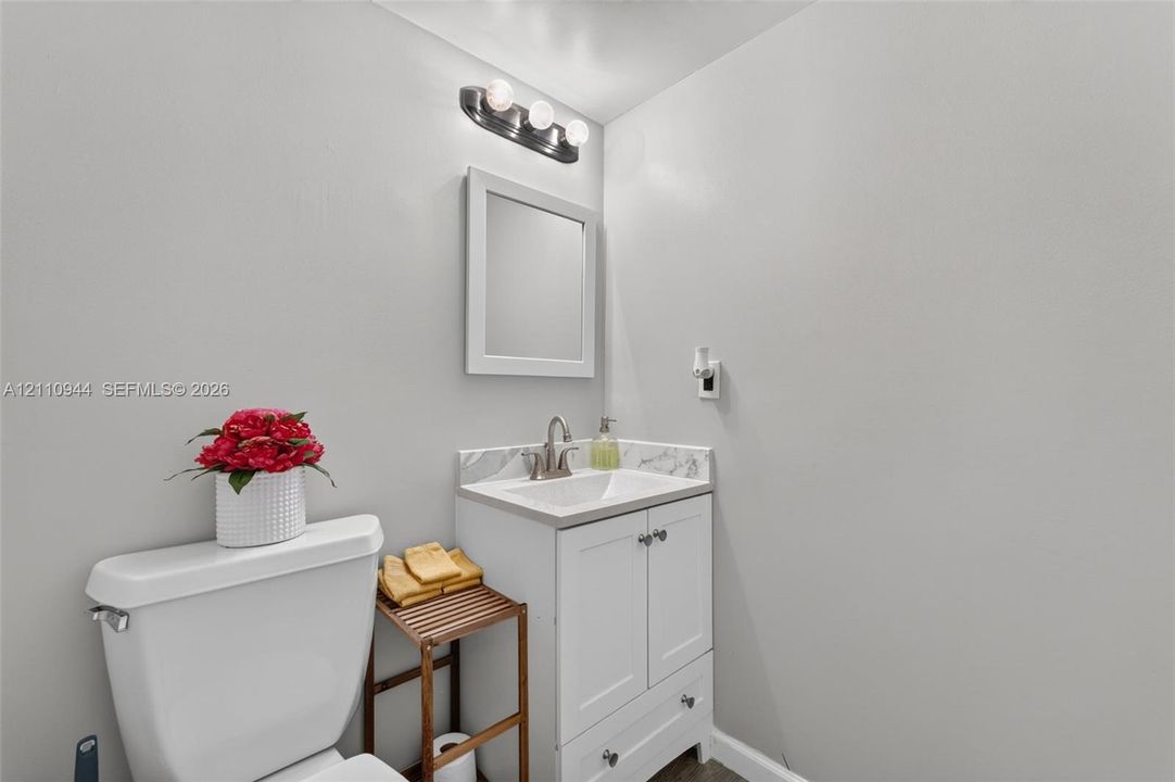 White vanity featuring a stone-look countertop, integrated basin, brushed metal faucet, framed wall mirror, and three-bulb vanity light fixture