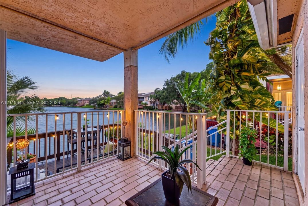 Covered terrace with masonry tile flooring, white metal balustrades, and direct water frontage
