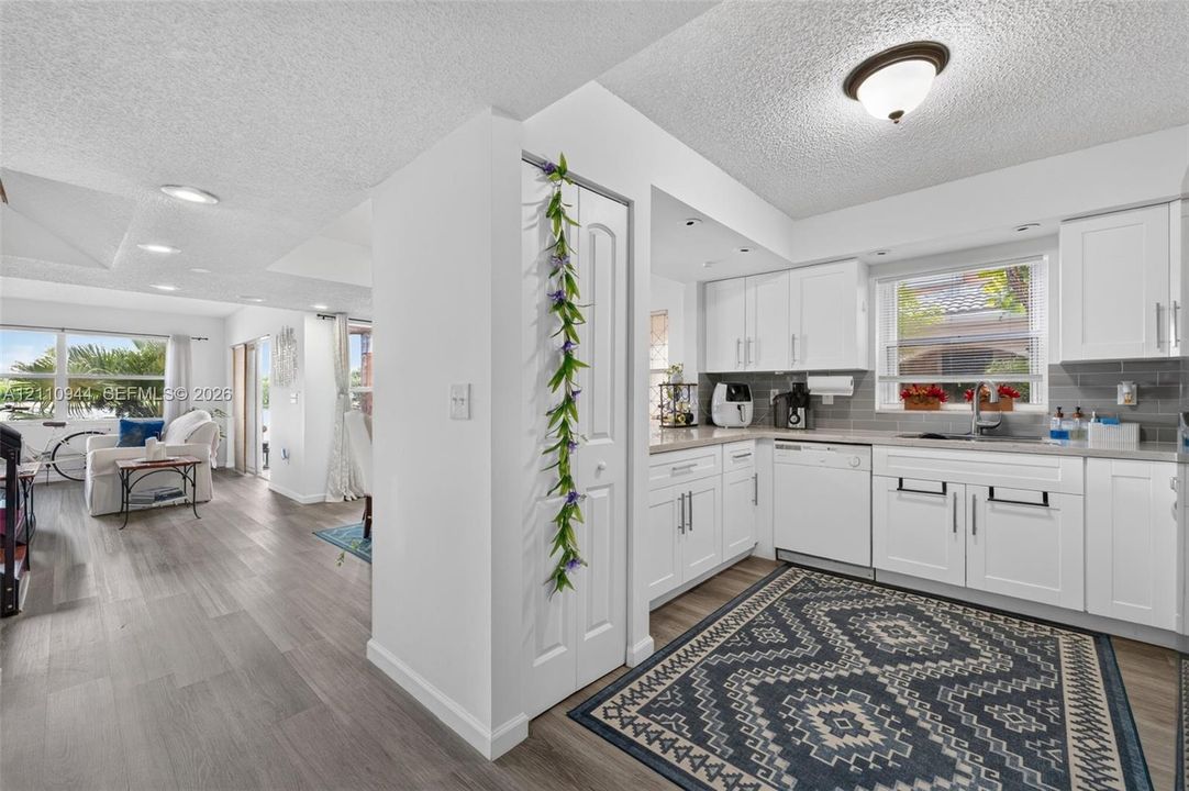 Kitchen featuring white cabinetry, grey tile backsplash, dishwasher, and wood-finish flooring