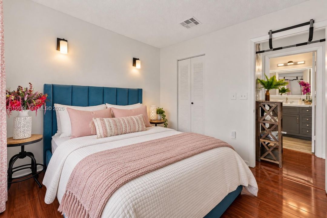 Wood-finish flooring, dual wall-mounted light fixtures, closet with louvered doors, and bathroom featuring a vanity with dark cabinetry