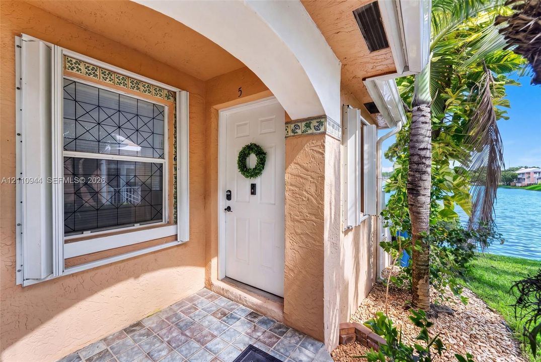 Covered entryway featuring textured stucco exterior, decorative tile accents, grid-pattern window, and tile flooring