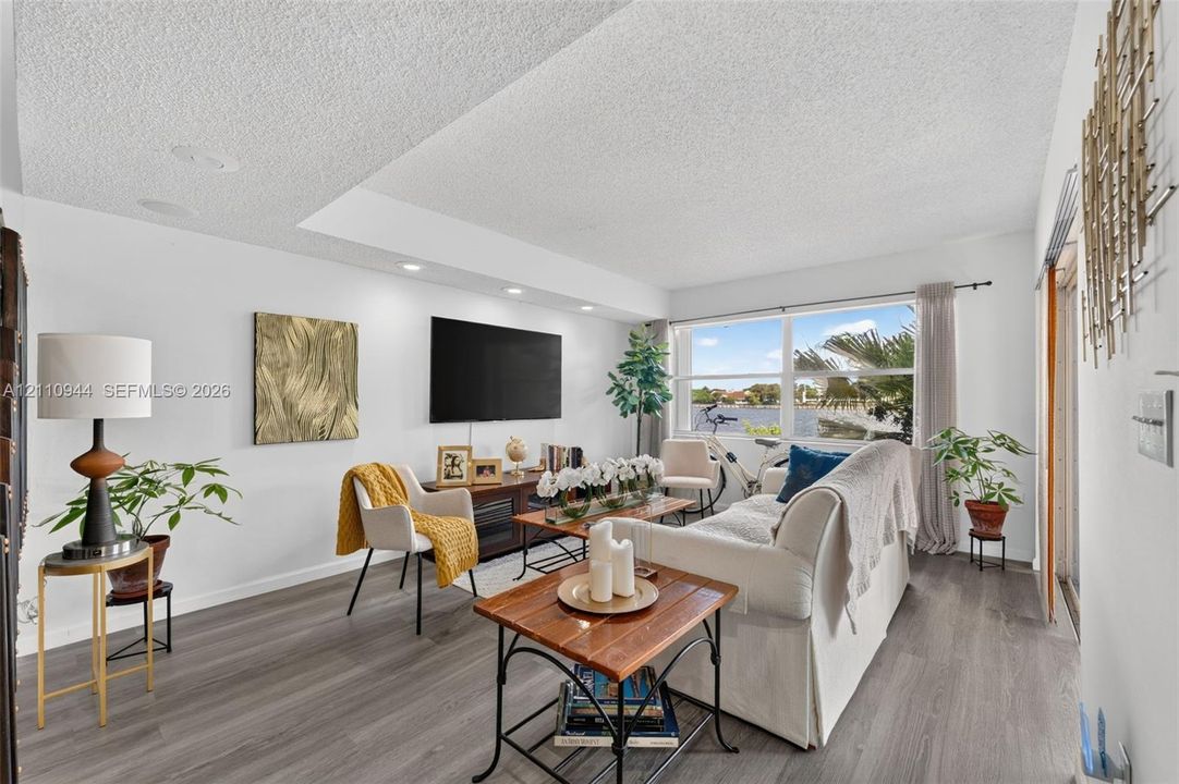 Living area featuring wood-finish flooring, recessed lighting, a dropped ceiling detail, and a large window overlooking the water