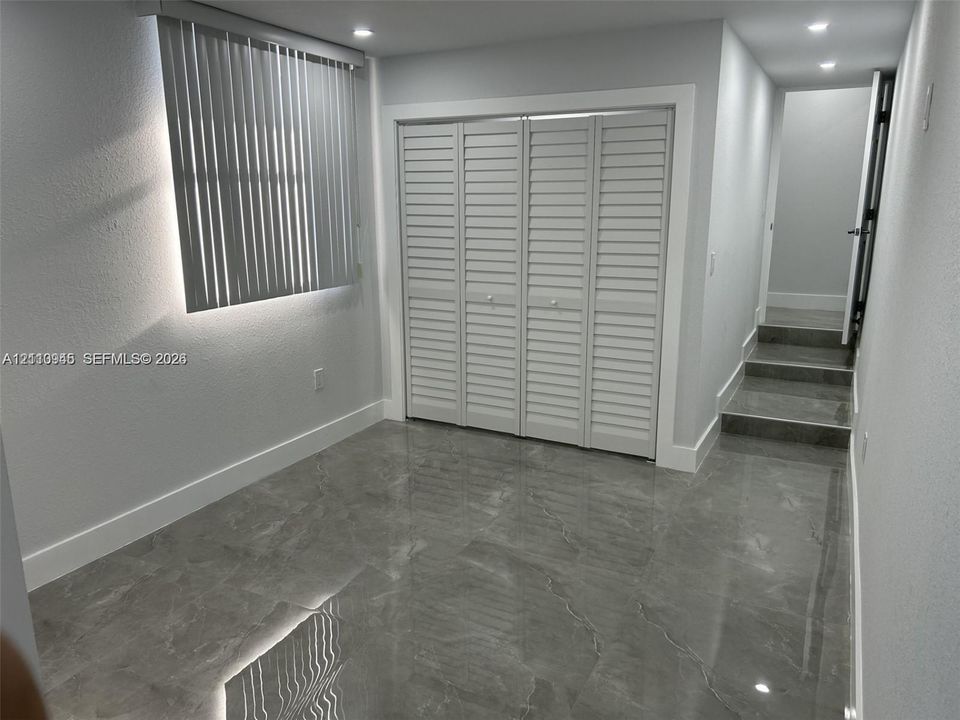 Room with large-format grey tile flooring, recessed ceiling lighting, louvered bi-fold closet doors, and horizontal slat window blinds