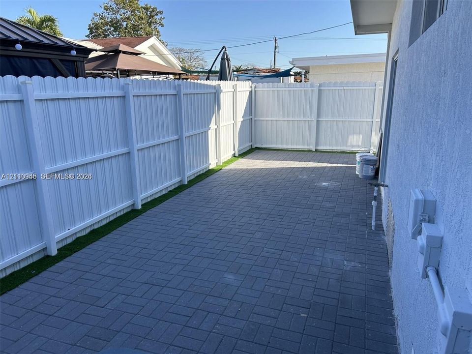Outdoor space featuring a grey paver patio, white vinyl privacy fencing, and an integrated turf border