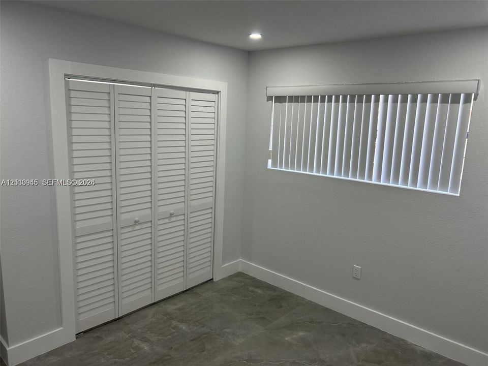 Room featuring neutral-toned walls, tile flooring, louvered bi-fold closet doors, and a window equipped with vertical blinds
