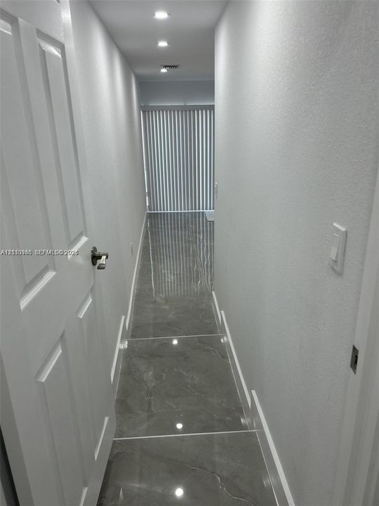 Hallway featuring large-format grey tile flooring, recessed ceiling lighting, and vertical blinds over a sliding glass door