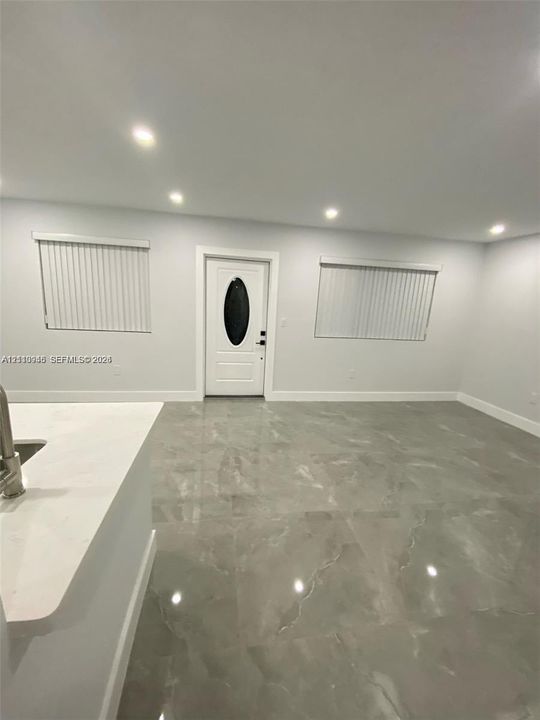 Large-format tile flooring, recessed ceiling lighting, and a white front entry door with an oval glass inset, complemented by neutral walls and window treatments
