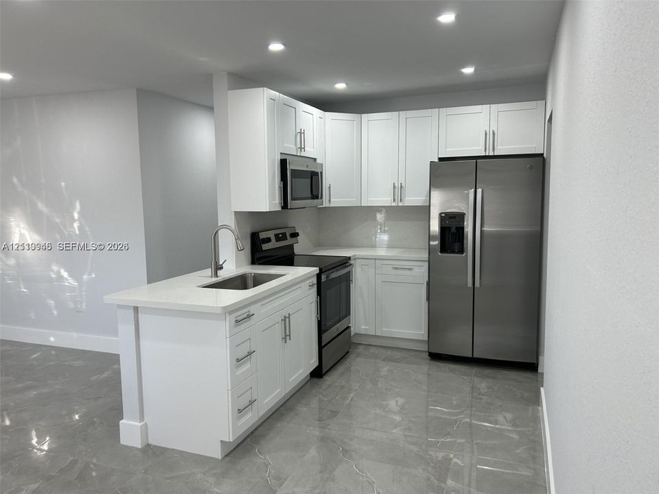 Kitchen featuring white cabinetry, solid-surface countertops, stainless steel appliances, a undermount sink with a gooseneck faucet, and stone-finish flooring