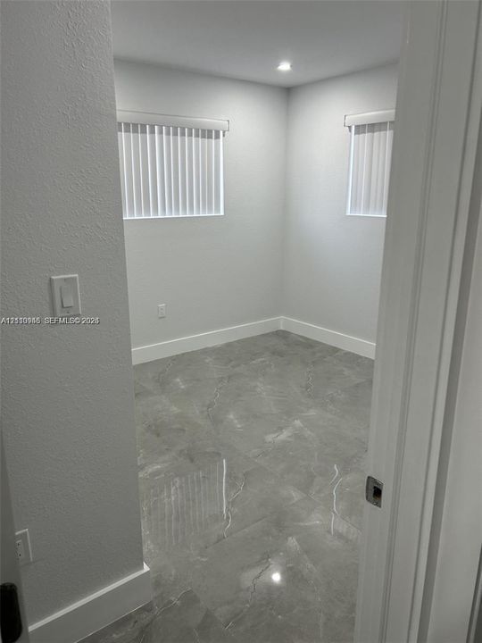 Interior space featuring large-format grey stone-finish tile flooring, neutral walls, two windows with vertical blinds, and recessed lighting