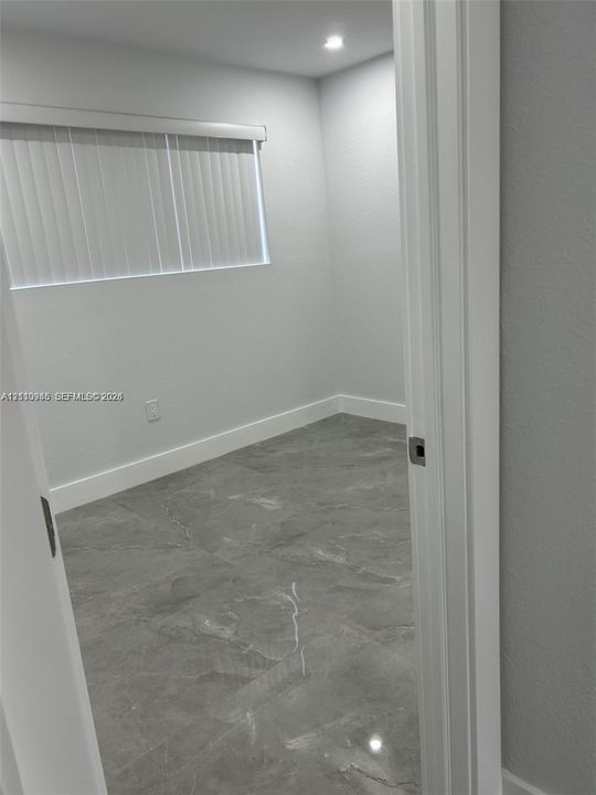 Interior space featuring large-format grey tile flooring, neutral wall tones, recessed lighting, and a horizontal window with vertical blinds