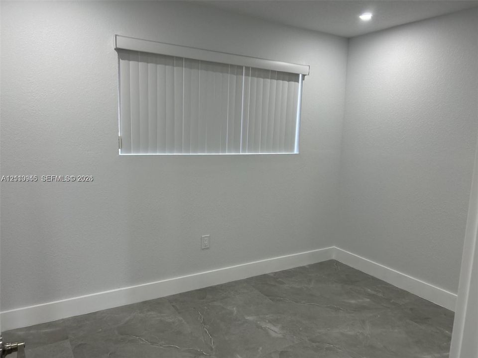 Neutral-toned interior featuring large-format tile flooring, recessed ceiling lighting, and a single window with vertical blinds