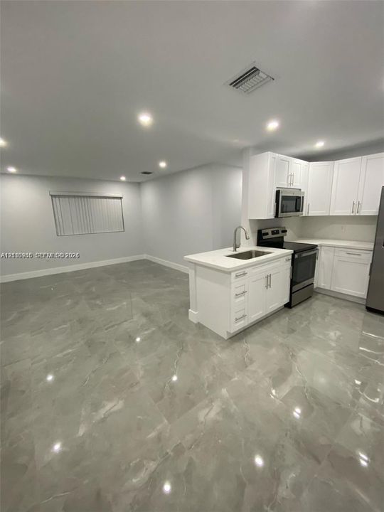 Kitchen area featuring white shaker-style cabinetry, a central island with an undermount sink, recessed lighting, and large-format porcelain tile flooring