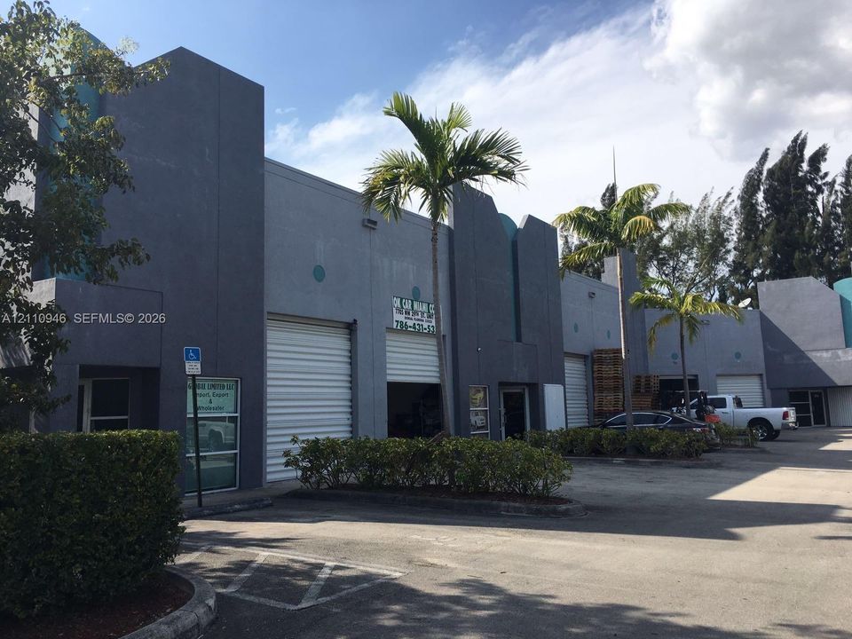 Commercial structure featuring multi-bay roll-up doors, concrete exterior facade, and paved parking area with perimeter landscaping