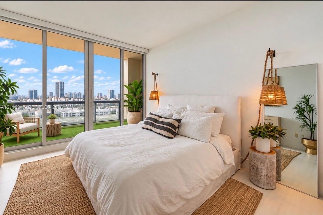 Floor-to-ceiling glass sliding doors, private balcony, neutral-toned tile flooring, and wall-mounted light fixtures