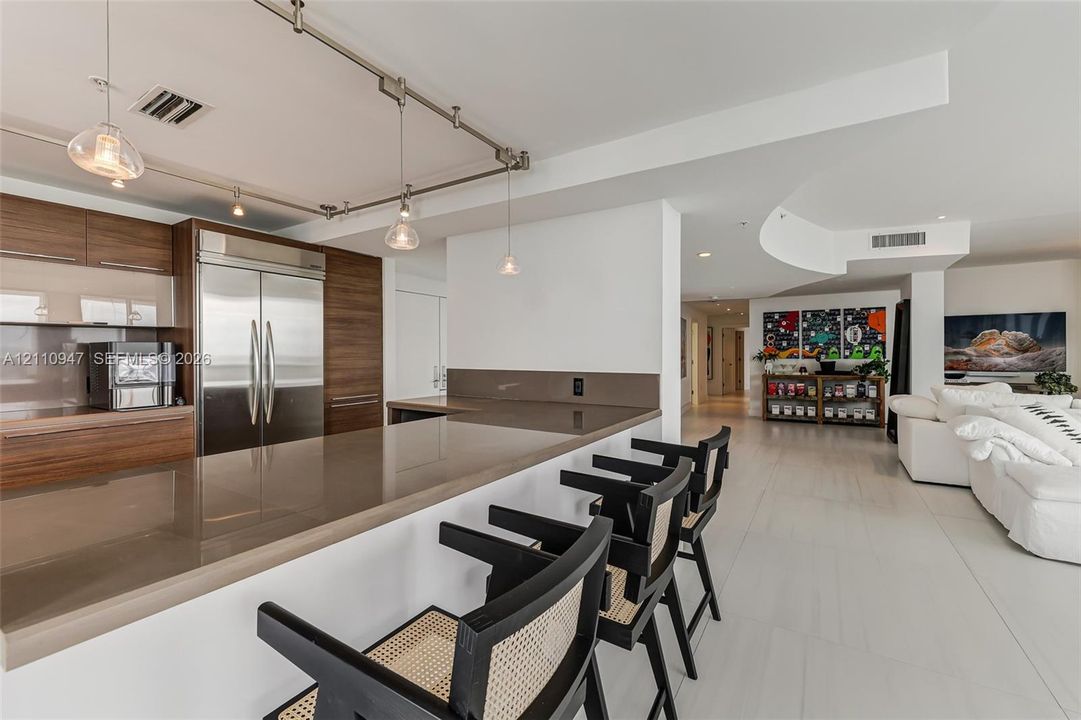 Kitchen featuring flat-panel wood cabinetry, integrated stainless steel refrigerator, solid-surface countertops with breakfast bar seating, and overhead track lighting
