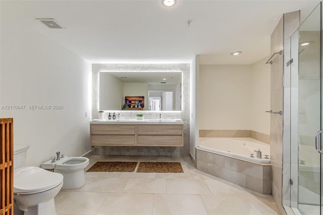 Floating wood-finish double vanity, integrated LED-backlit mirror, jetted soaking tub, walk-in glass-enclosed shower, and large-format tile flooring