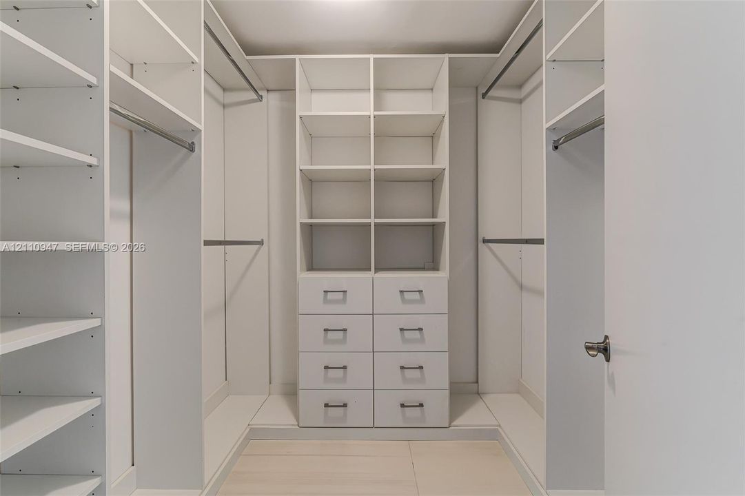 Custom reach-in closet featuring white built-in shelving, dual hanging rods, and a center tower with eight integrated drawers