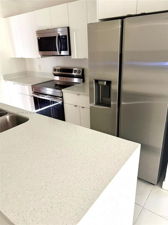 Kitchen featuring white flat-panel cabinetry, stone-finish countertops, stainless steel side-by-side refrigerator, matching stainless steel range, and built-in microwave