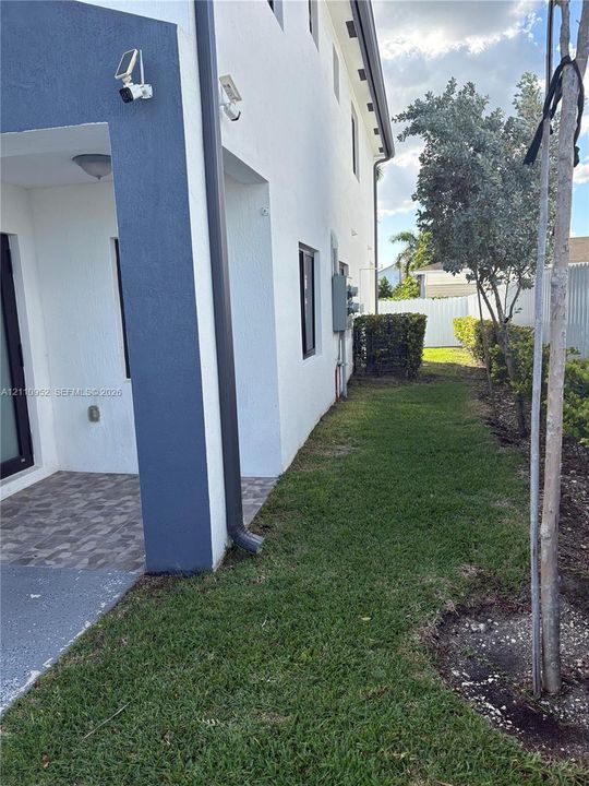 Stucco exterior side profile featuring a covered patio with patterned tile flooring, manicured lawn, and perimeter fence
