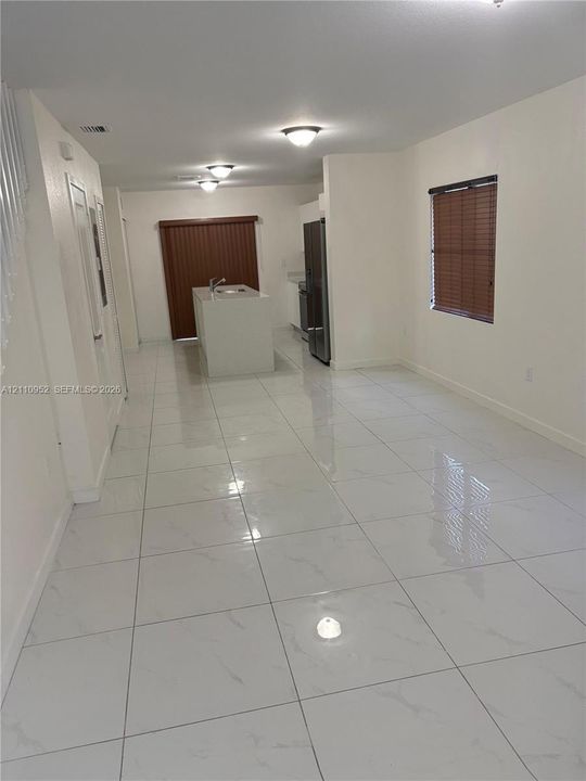 Large-format tile flooring with a light finish, central kitchen island with a built-in sink, stainless steel refrigerator, and recessed ceiling lighting