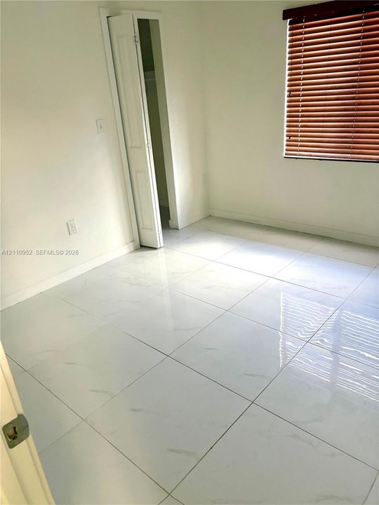 Large-format tile flooring with a light marbled finish, accompanied by a bi-fold closet door and horizontal slat window blinds