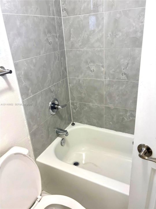 Full-height ceramic tile tub surround, integrated porcelain bathtub, and polished chrome hardware