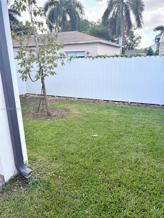 Backyard featuring a white scalloped-top privacy fence, manicured lawn, and mature foliage
