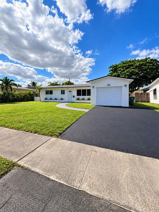 Single-story exterior featuring a white facade, attached one-car garage, asphalt driveway, curved concrete walkway, and manicured lawn