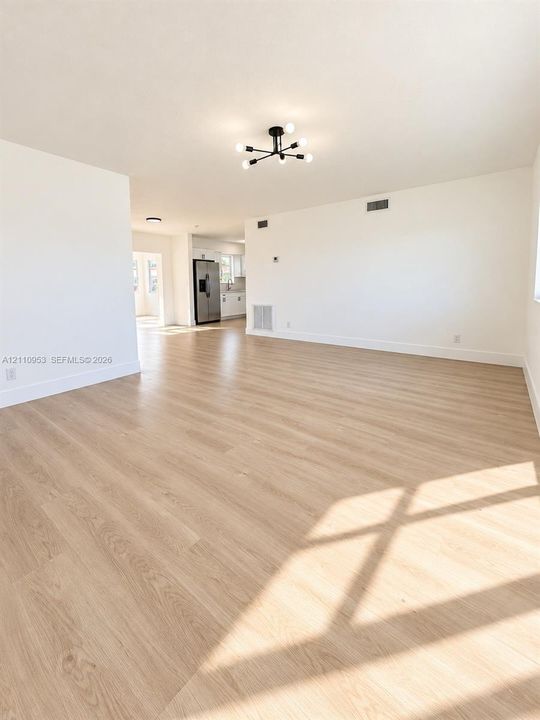 Open-concept interior featuring wood-finish flooring, a contemporary six-arm matte black chandelier, and neutral wall tones