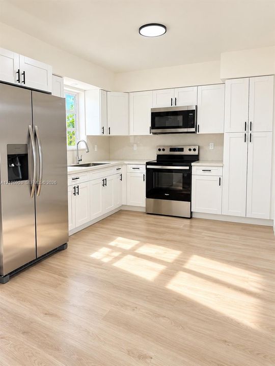 Kitchen featuring white shaker-style cabinetry, stainless steel appliances, light wood-finish flooring, and a single-basin undermount sink with a gooseneck faucet
