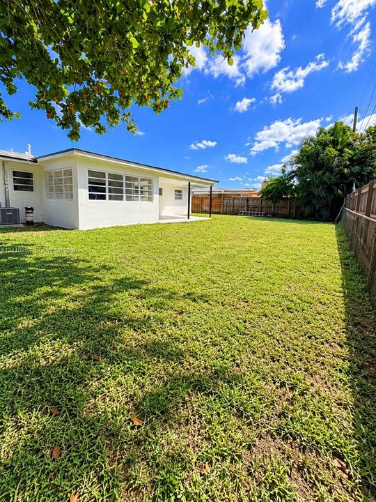 Expansive backyard featuring a large grass lawn, perimeter wood fencing, masonry boundary wall, and a covered patio area