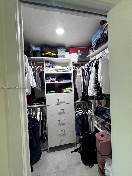 Walk-in closet featuring white built-in shelving, a five-drawer storage unit with metal pulls, dual-level hanging rods, and stone-finish flooring