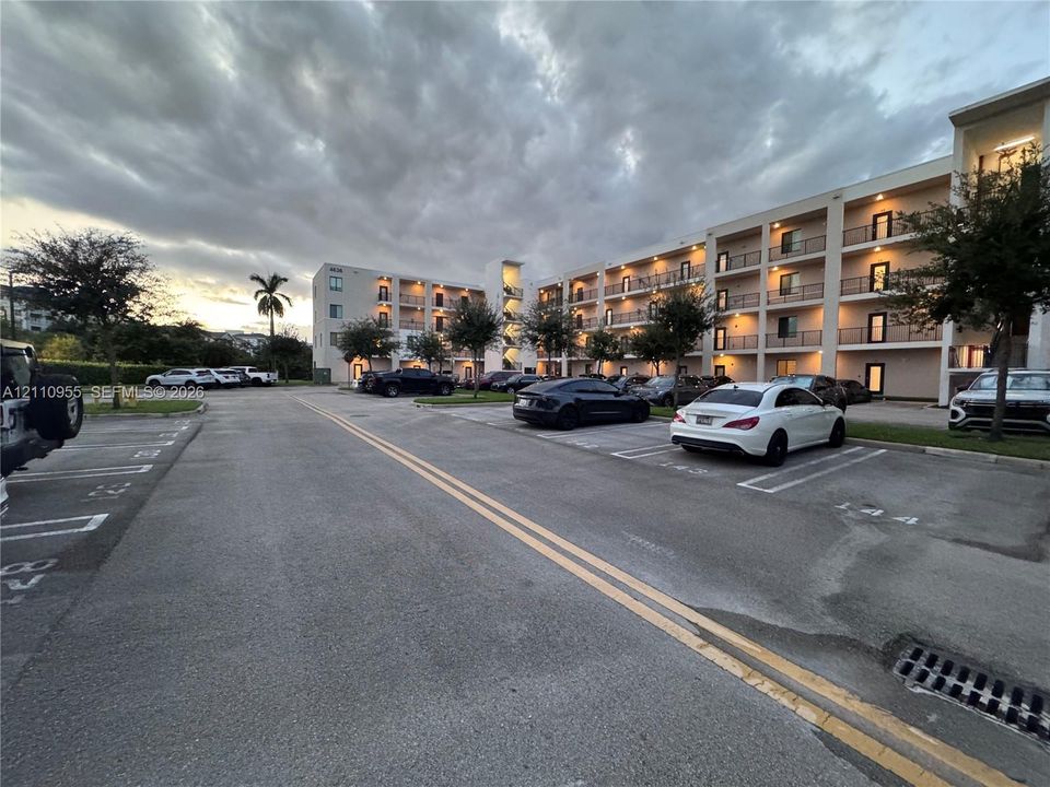 Multi-story residential building exterior featuring concrete facade, private recessed balconies, and paved surface parking