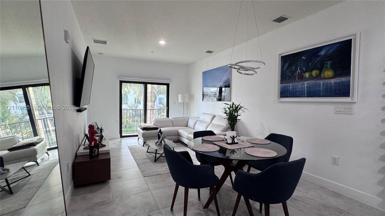 Open-concept interior featuring large-format tile flooring, a contemporary circular multi-ring pendant light, full-height wall mirror, and sliding glass doors leading to an exterior balcony